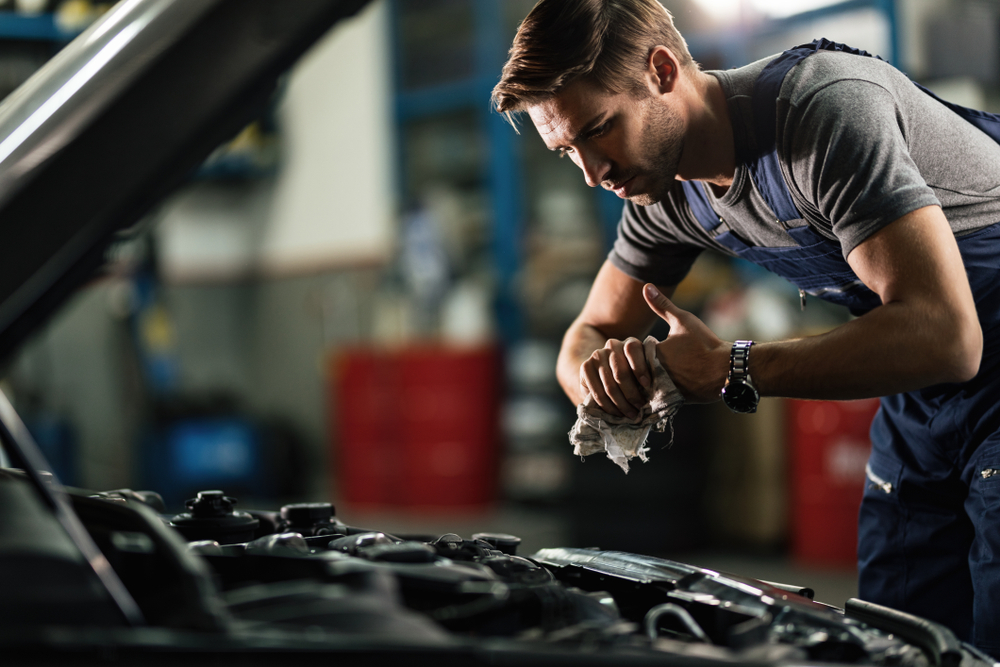 Young,mechanic,wiping,his,hands,while,repairing,car,engine,in